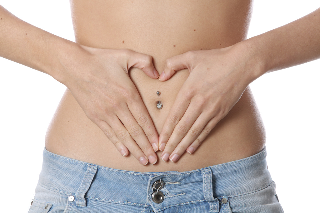 A woman wearing low, on the hip jeans, places her hands on her abdomen to form a heart shape round her navel