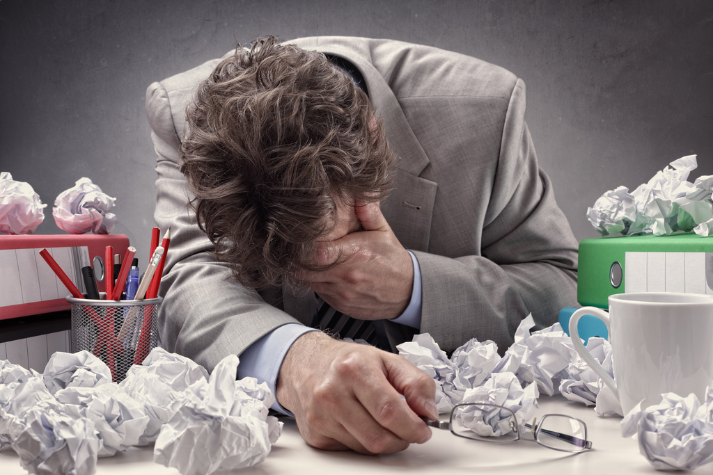 Overworked, depressed and exhausted office workers at his desk surrounded by a pile of work